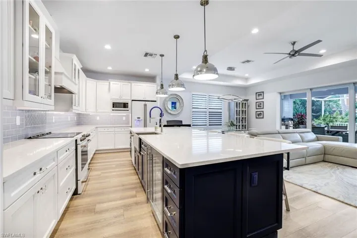Kitchen with hanging light fixtures, white cabinets, an island with sink, light wood-type flooring, and high end appliances