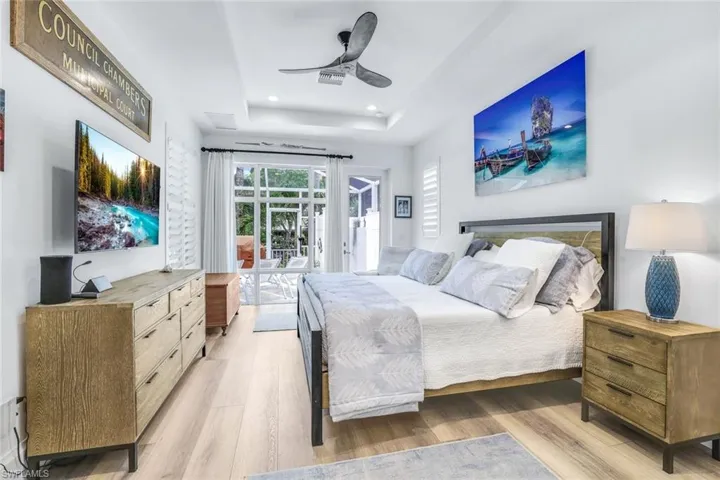 Bedroom featuring a tray ceiling, light hardwood / wood-style flooring, access to exterior, and ceiling fan