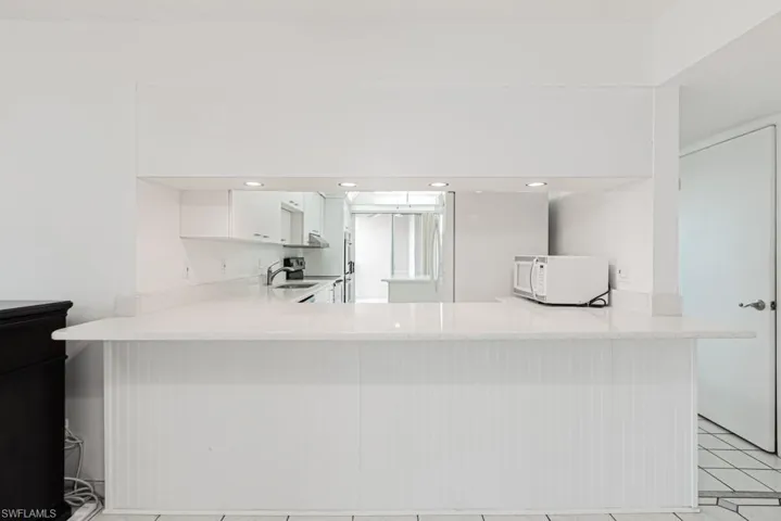 Kitchen featuring white cabinetry, kitchen peninsula, light stone counters, sink, and light tile flooring