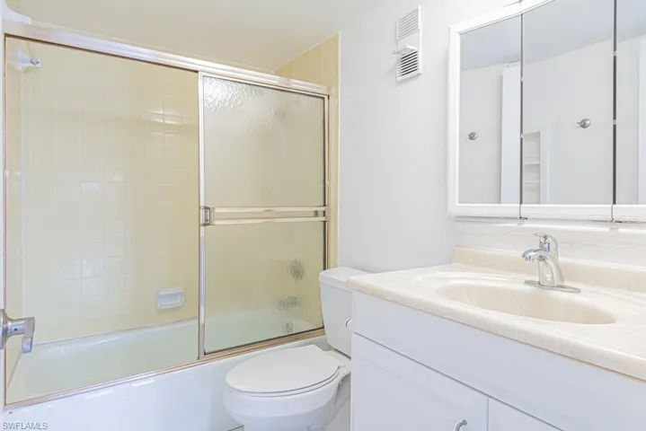 Full bathroom featuring combined bath / shower with glass door, toilet, and vanity with extensive cabinet space