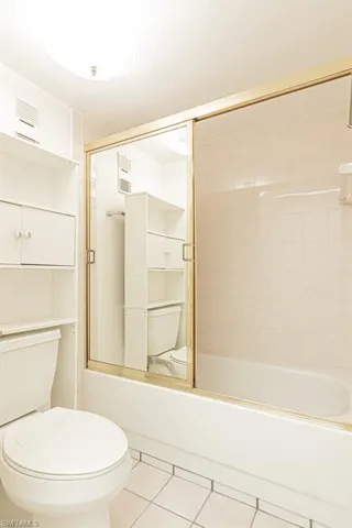 Bathroom with tile flooring, shower / bath combination with glass door, and toilet