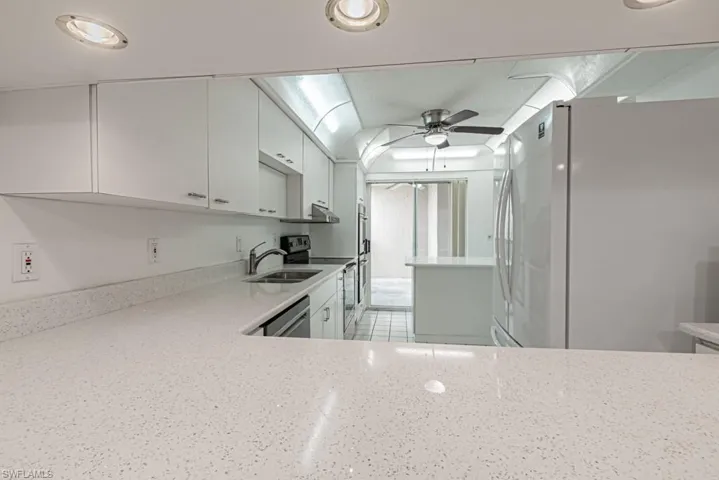 Kitchen featuring ceiling fan, light tile flooring, sink, white cabinets, and appliances with stainless steel finishes