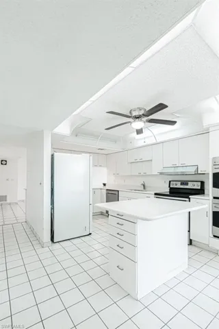 Kitchen with a kitchen island, stainless steel appliances, white cabinets, light tile flooring, and ceiling fan