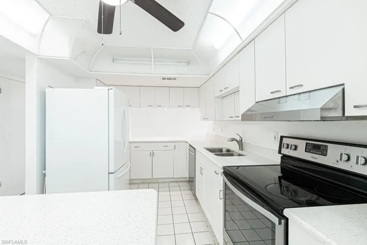 Kitchen featuring ceiling fan, stainless steel appliances, light tile floors, sink, and white cabinetry