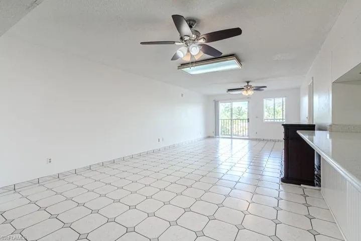 Tiled empty room with ceiling fan, a textured ceiling, and a skylight
