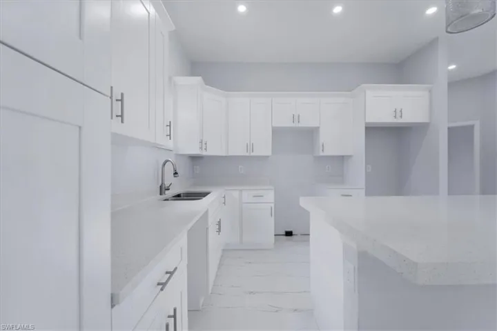 Kitchen with white cabinetry, light stone counters, and sink