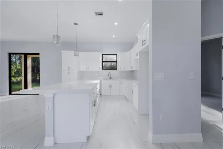 Kitchen featuring sink, a kitchen island, pendant lighting, white cabinets, and light stone counters
