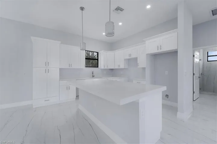 Kitchen with white cabinets, sink, hanging light fixtures, and a kitchen island