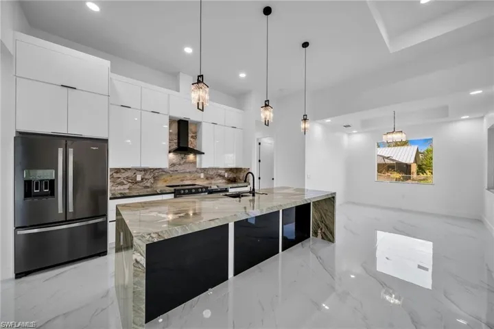 Kitchen featuring stainless steel appliances, wall chimney range hood, modern cabinets, a sink, and light marble finish flooring