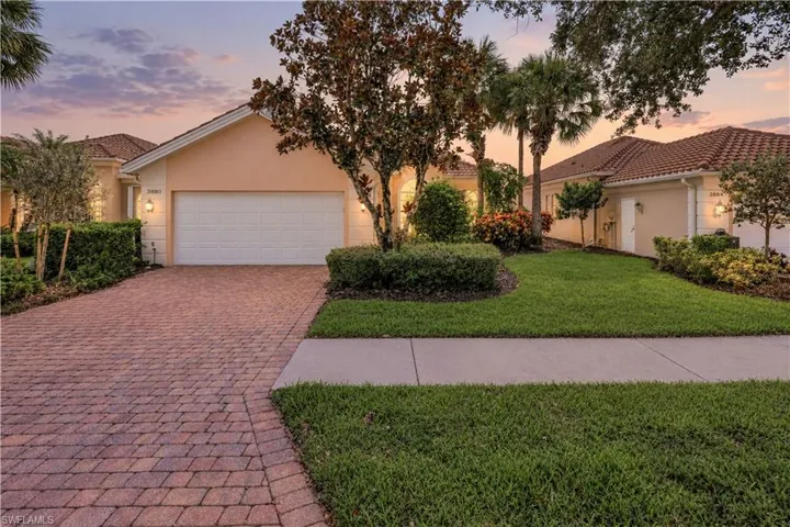 Stucco exterior featuring a tile roof, brick-paver driveway, and manicured landscaping