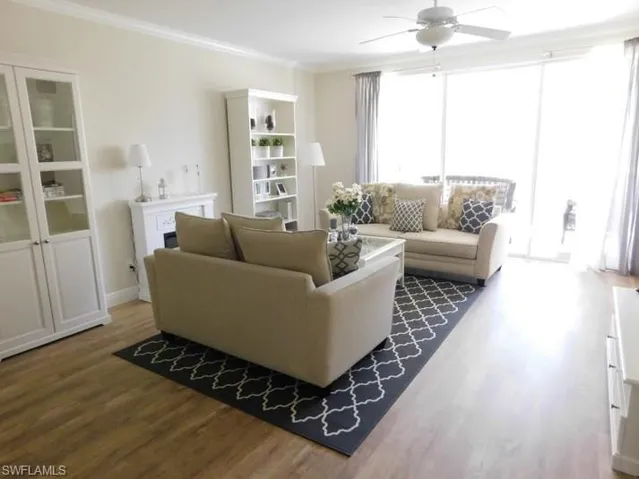 Living area with a ceiling fan, wood finished floors, crown molding, and a fireplace