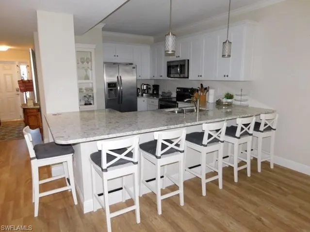 Kitchen featuring stainless steel appliances, a peninsula, light wood-style flooring, light stone counters, and white cabinetry
