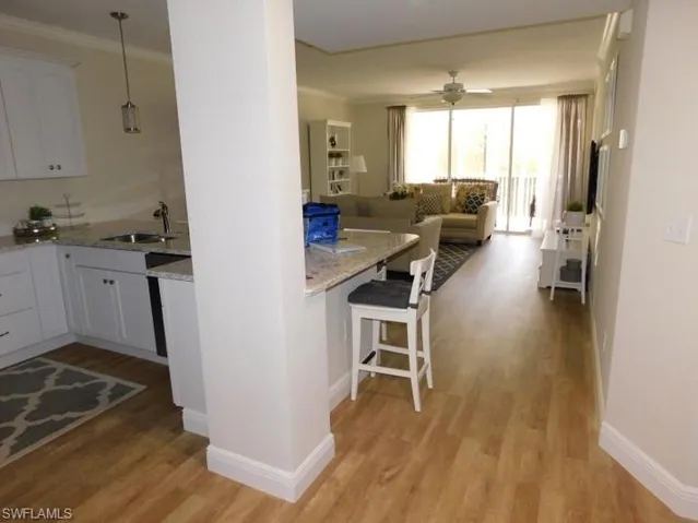 Kitchen featuring light wood finished floors, ornamental molding, light stone countertops, a breakfast bar, and open floor plan