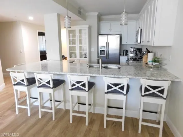 Kitchen featuring appliances with stainless steel finishes, a peninsula, light wood-style floors, light stone countertops, and crown molding