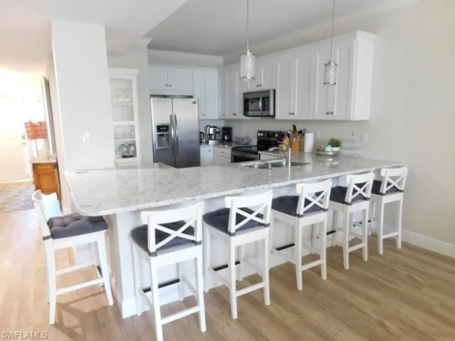 Kitchen featuring stainless steel appliances, a peninsula, light wood-style flooring, light stone countertops, and crown molding
