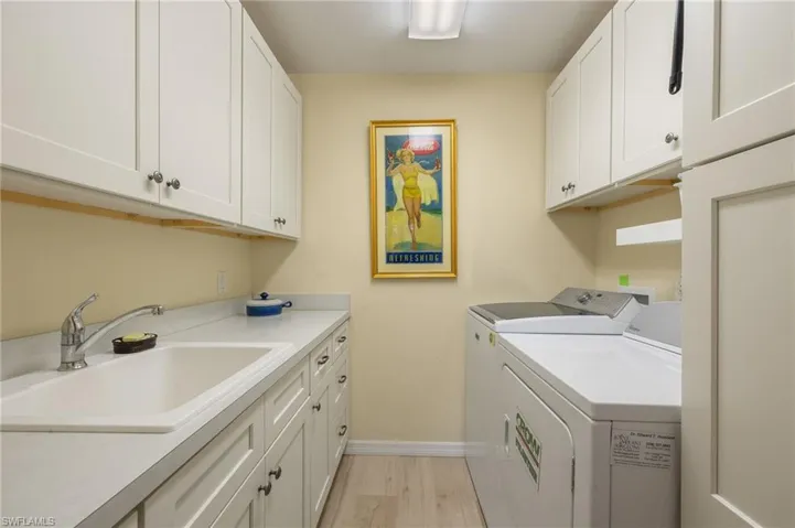 Laundry area featuring cabinets, separate washer and dryer, sink, and light wood-type flooring