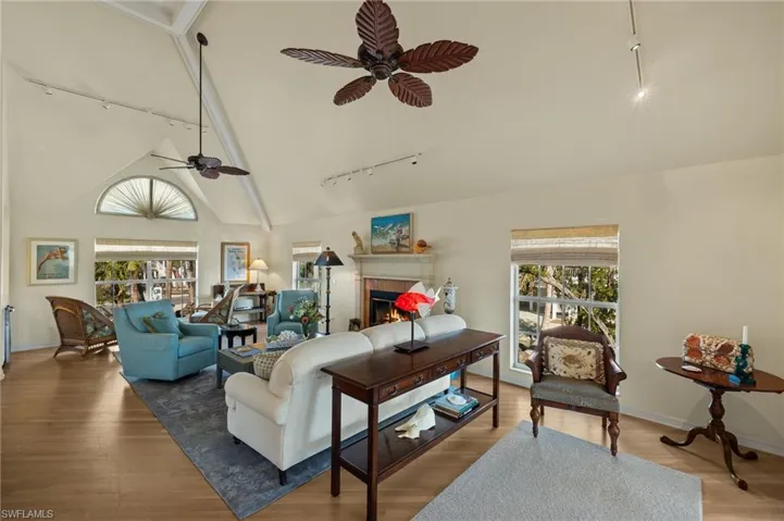 Living room featuring hardwood / wood-style flooring, a tile fireplace, ceiling fan, high vaulted ceiling, and track lighting