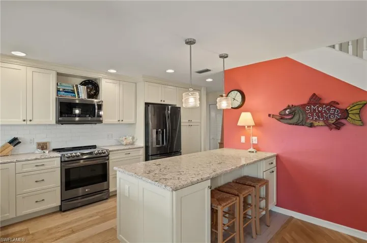 Kitchen featuring light stone counters, decorative backsplash, appliances with stainless steel finishes, and hanging light fixtures