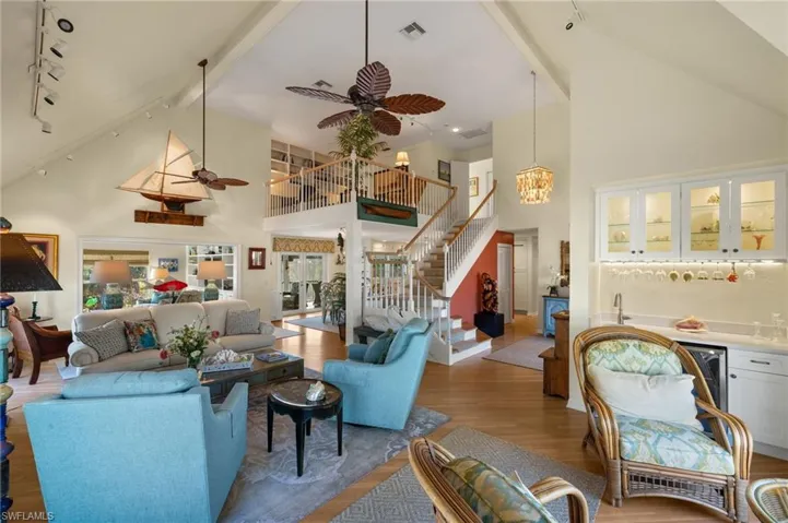 Living room featuring beamed ceiling, indoor bar, ceiling fan with notable chandelier, and hardwood / wood-style floors