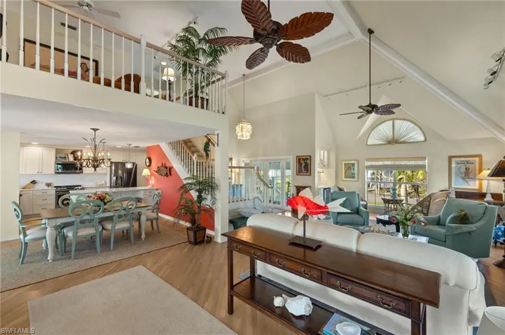 Living room featuring high vaulted ceiling, rail lighting, ceiling fan with notable chandelier, and light hardwood / wood-style flooring