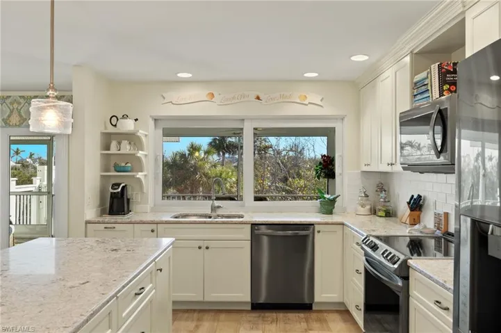 Kitchen with sink, light stone counters, tasteful backsplash, decorative light fixtures, and appliances with stainless steel finishes