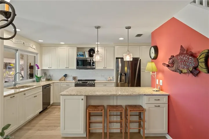 Kitchen featuring light stone counters, backsplash, pendant lighting, and appliances with stainless steel finishes