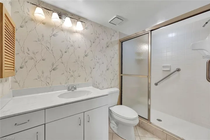 Guest Bathroom featuring wallpapered walls, vanity, a stall shower, and light tile patterned flooring