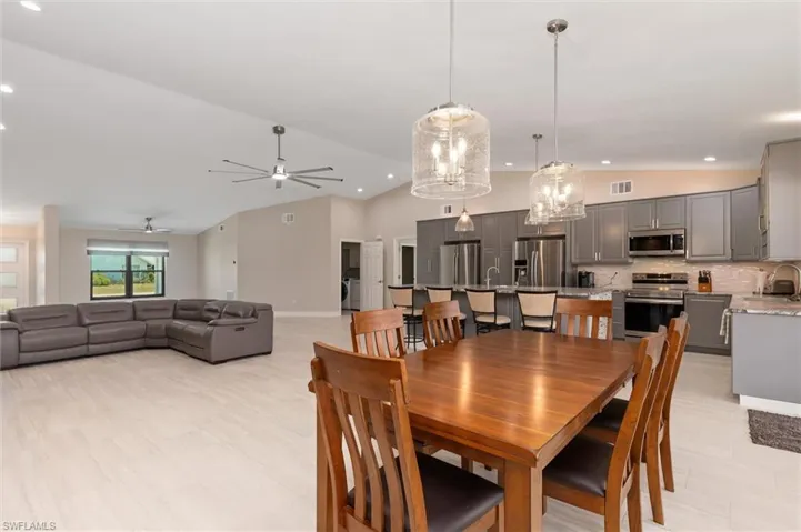 Dining space featuring high vaulted ceiling, baseboards, ceiling fan with notable chandelier, visible vents, and recessed lighting