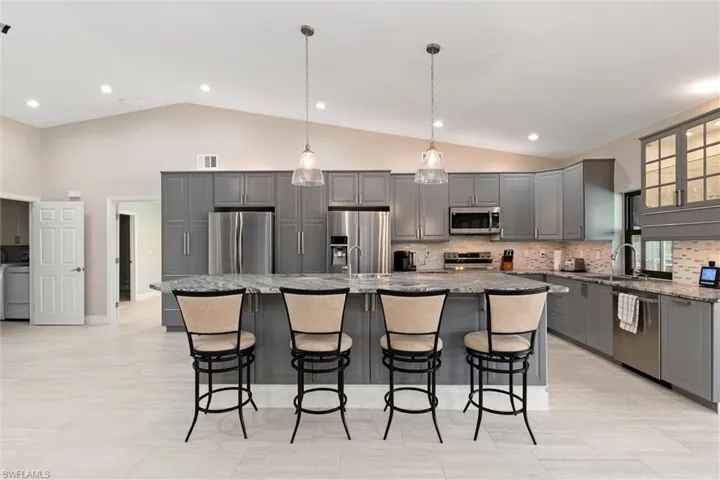 Kitchen with dark stone counters, a sink, stainless steel appliances, and gray cabinetry