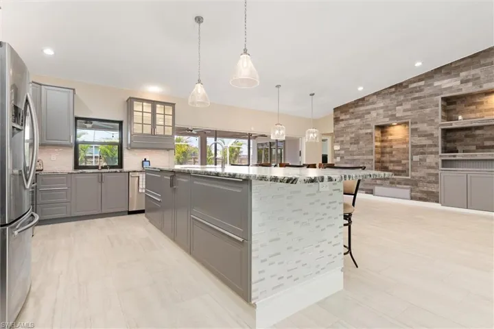 Kitchen with vaulted ceiling, gray cabinets, light stone countertops, stainless steel appliances, and decorative backsplash