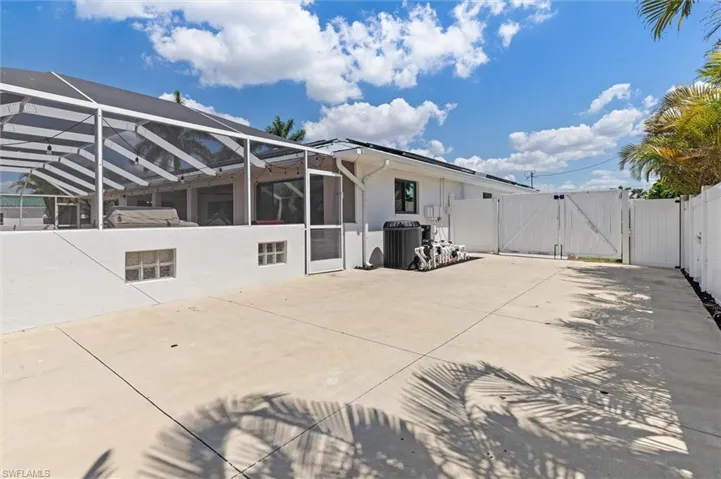 Rear view of property featuring stucco siding, fence, central AC unit, a gate, and a patio area