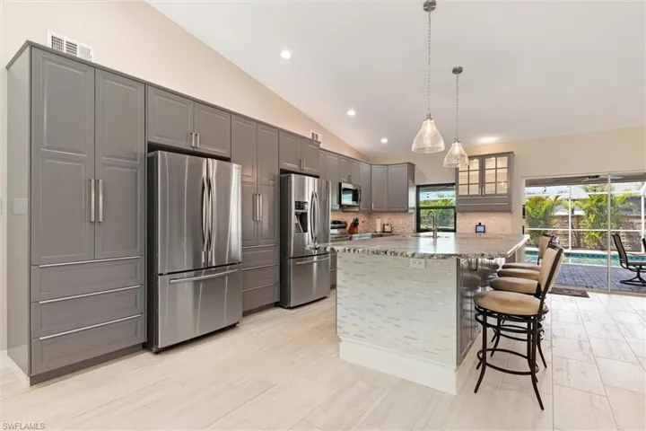 Kitchen with stainless steel appliances, lofted ceiling, a sink, gray cabinetry, and backsplash