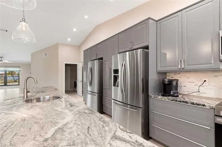 Kitchen with freestanding refrigerator, a sink, stainless steel refrigerator with ice dispenser, and gray cabinetry