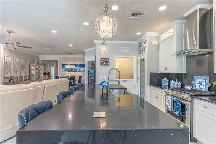Kitchen with wall chimney range hood, sink, stainless steel range, and an island with sink