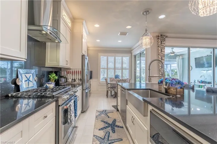 Kitchen with wall chimney range hood, stainless steel appliances, ceiling fan with notable chandelier, ornamental molding, and backsplash