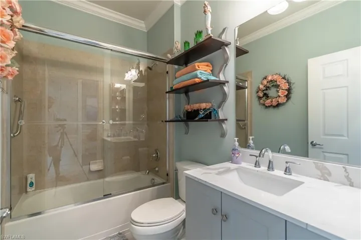 Full bathroom with combined bath / shower with glass door, toilet, vanity, and ornamental molding