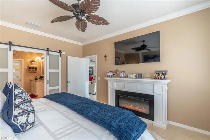 Bedroom with a barn door, connected bathroom, ceiling fan, and crown molding