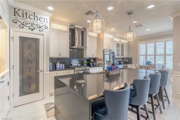 Kitchen featuring tasteful backsplash, wall chimney range hood, hanging light fixtures, high end range, and an island with sink