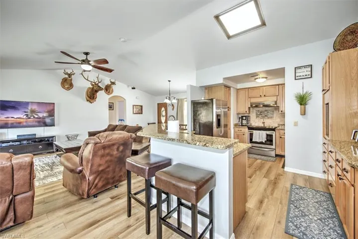 Kitchen featuring tasteful backsplash, light stone counters, vaulted ceiling, appliances with stainless steel finishes, and light wood-type flooring