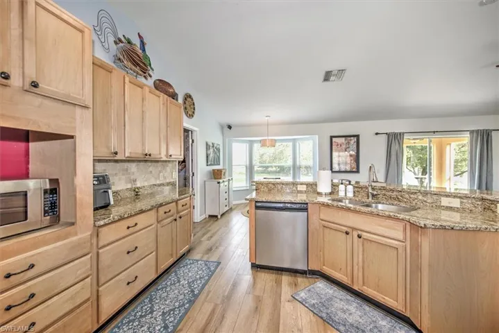 Kitchen with sink, stainless steel appliances, tasteful backsplash, light brown cabinetry, and light wood-type flooring