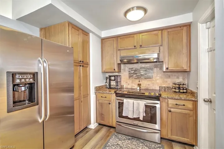 Kitchen featuring light hardwood / wood-style flooring, decorative backsplash, range hood, light stone counters, and stainless steel appliances