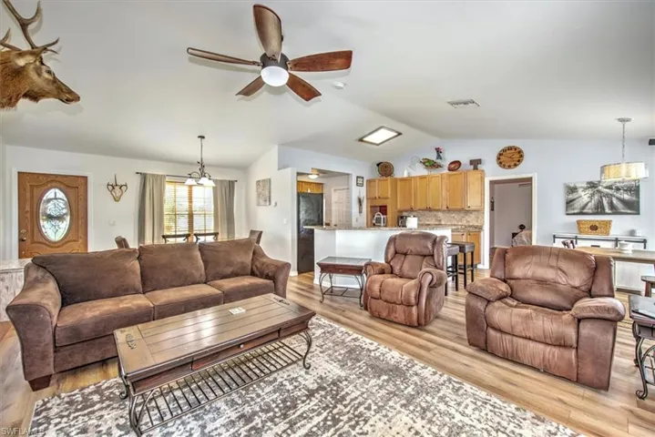 Living room with ceiling fan with notable chandelier, light wood-type flooring, and lofted ceiling