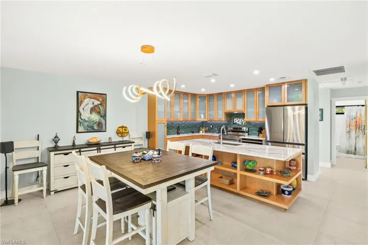 Kitchen featuring appliances with stainless steel finishes, open shelves, a center island with sink, decorative backsplash, and glass insert cabinets