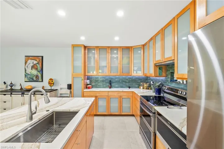 Kitchen featuring appliances with stainless steel finishes, decorative backsplash, glass insert cabinets, light stone countertops, and light tile patterned flooring