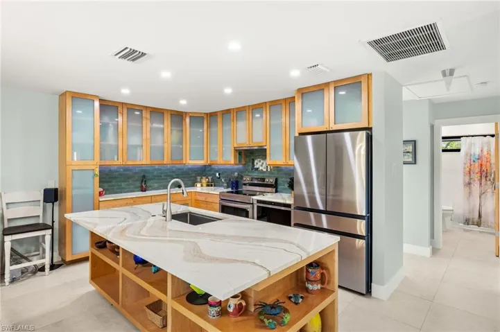 Kitchen featuring appliances with stainless steel finishes, open shelves, a center island with sink, tasteful backsplash, and light stone counters