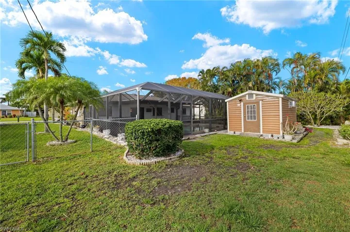Back of house featuring an outdoor structure, fence, a lawn, and a lanai