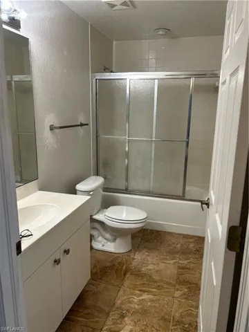 Bathroom featuring a textured wall, vanity, and combined bath / shower with glass door