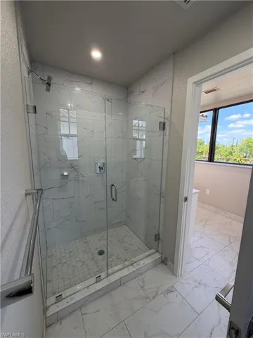 The bathroom features a spacious glass-enclosed shower with white marble-style tiled walls and a tiled floor