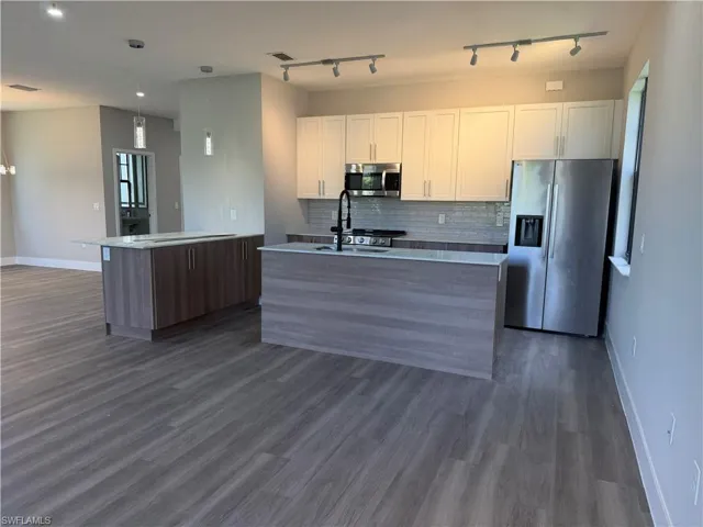 Contemporary kitchen featuring two islands, white cabinetry, stainless steel appliances, and track lighting