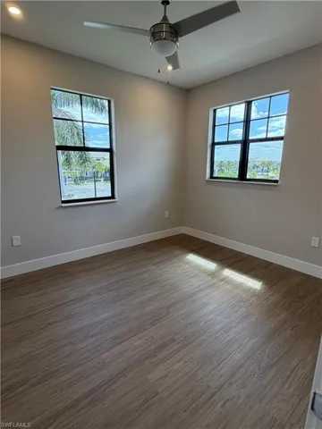 This room features durable plank flooring, two windows with views of the surrounding area, and a ceiling fan with integrated lighting